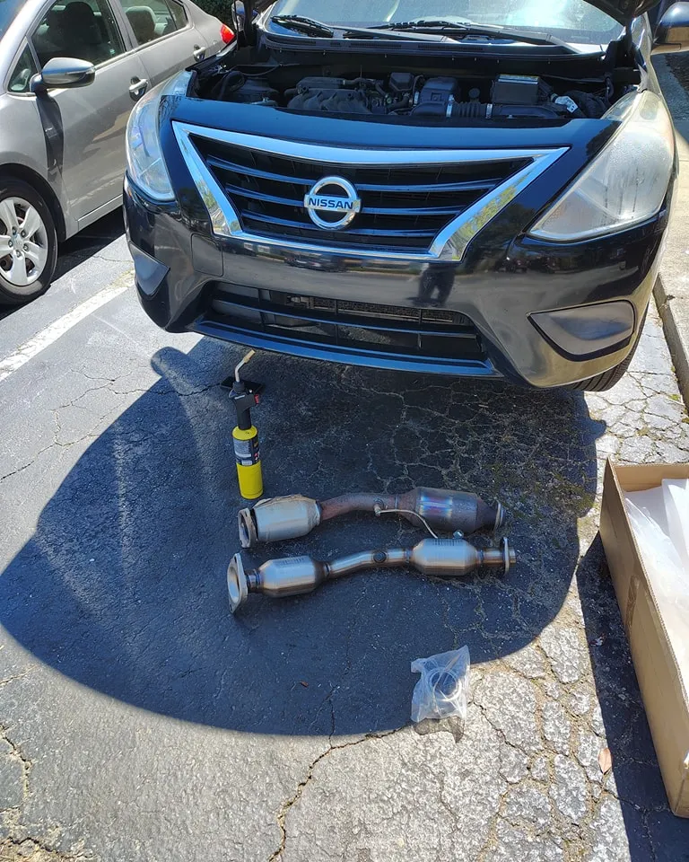 Replacement exhaust components prepared beside a Nissan sedan