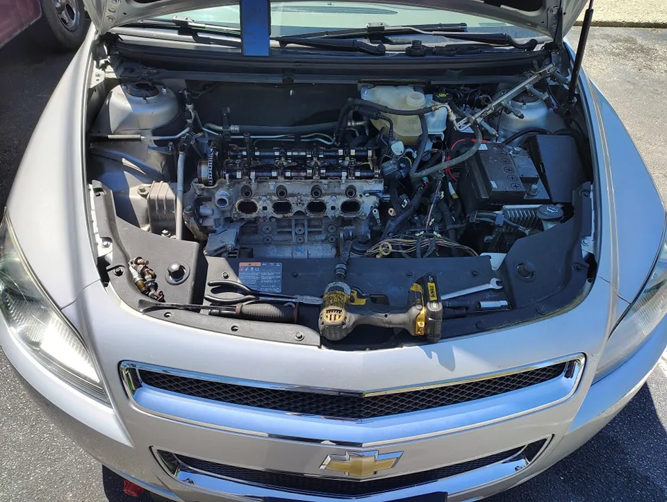 Engine repair in progress under the hood of a silver Chevrolet